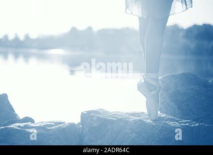 Belles jambes d'une ballerine sur le bord de la mer sur les pierres, au coucher du soleil, dans le mode teinté couleur de l'année. 2020 pantone bleu classique Banque D'Images