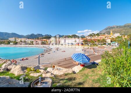 Les touristes et les habitants profitez d'une journée ensoleillée sur la côte d'Azur comme ils vous détendre sur la plage de sable de plage Méditerranéenne Fossan à Menton, France Banque D'Images