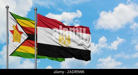 Le Zimbabwe et de brandir le drapeau de l'Égypte dans le vent contre ciel bleu nuageux blanc ensemble. Concept de diplomatie, de relations internationales. Banque D'Images