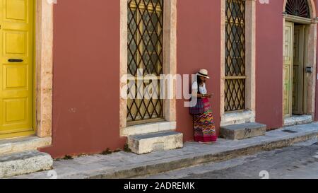 Asian Woman in white t-shirt à Athènes en white hat et sarong leaning against wall avec de grandes fenêtres à Plaka Banque D'Images