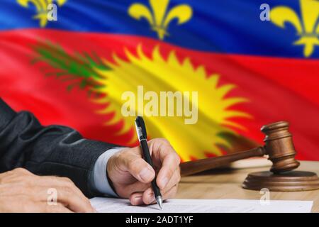 Le juge écrit sur papier dans la salle d'audience avec la Guadeloupe drapeau arrière-plan. Wooden gavel d'égalité thème et concept juridique. Banque D'Images