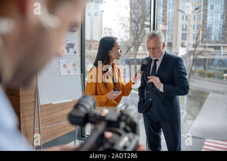 Jeune femme journaliste tenant un microphone au cours d'interview Banque D'Images