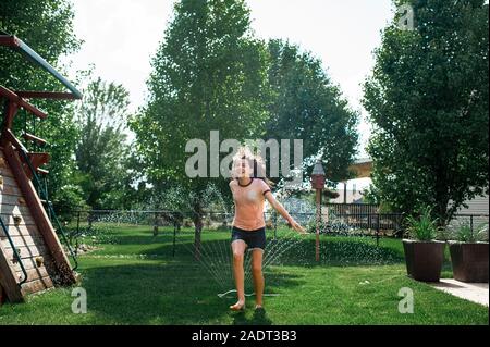 Le Tween girls laughing comme elle passe à travers les vêtements avec gicleurs sur Banque D'Images