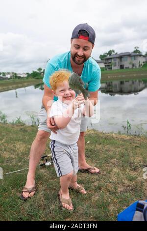 Père sourire tout-petits fils aide à maintenir en place un poisson qu'il a obtenu à un étang Banque D'Images