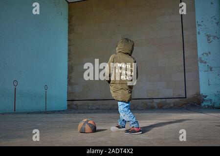 Garçon avec les mains dans les poches de son côté d'un ballon de basket-ball dégonflé. Banque D'Images