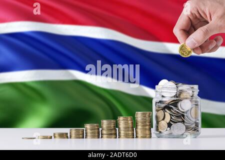 Business man holding coins mise en verre, de brandir le drapeau de la Gambie dans l'arrière-plan. Concept de la finance et des affaires. L'économie d'argent. Banque D'Images