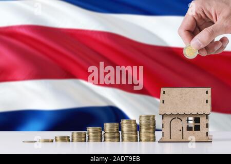 Man holding coins mise en maison en bois tirelire, de brandir le drapeau du Costa Rica dans l'arrière-plan. Économiser de l'argent pour prêt hypothécaire. Banque D'Images