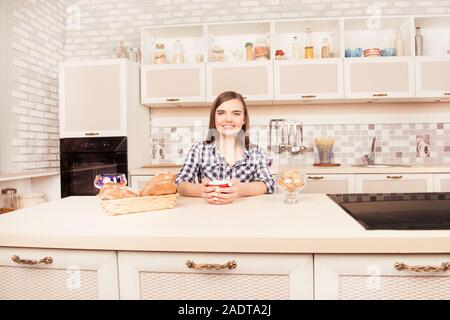 Belle jeune fille assise dans la cuisine avec une tasse de thé Banque D'Images