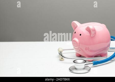 Pink piggy bank et stéthoscope sur un fond gris. Concept de comment économiser sur l'assurance maladie ou une assurance personnelle. L'espace de copie pour le texte Banque D'Images