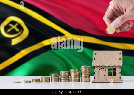 Man holding coins mise en maison en bois tirelire, de brandir le drapeau de Vanuatu dans l'arrière-plan. Économiser de l'argent pour prêt hypothécaire. Banque D'Images