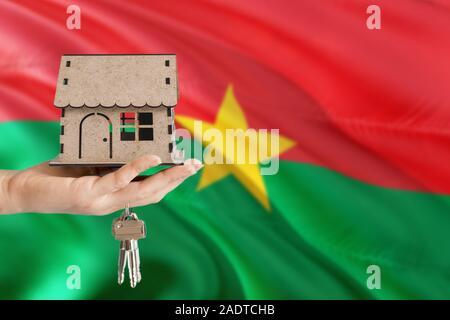 Woman hand holding maison en bois et les touches avec la main. Burkina Faso drapeau avec concept de louer, achat, assurance, immobilier, construction maison écologique. Banque D'Images