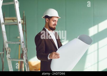 Homme barbu contremaître dans un casque blanc dans une chambre sur un site de construction Banque D'Images