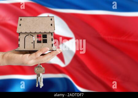 Woman hand holding maison en bois et les touches avec la main. La Corée du Nord drapeau avec concept de louer, achat, assurance, immobilier, construction maison écologique. Banque D'Images