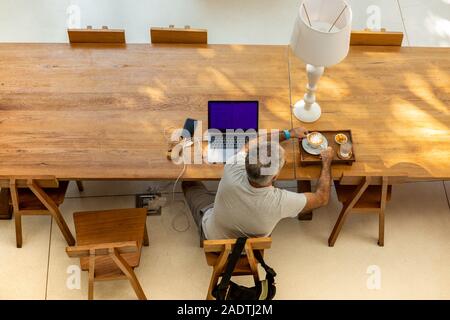 Vue de dessus de l'homme retraite holding coffee et working on laptop in cafe. Banque D'Images