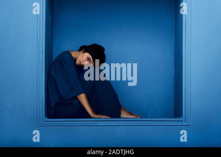 Fashion photo de belle jeune femme assise dans une niche sur fond bleu. Studio shot. Banque D'Images