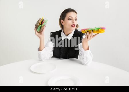 Nous sommes ce que nous mangeons. Femme mange burger et hot-dog en plastique, eco concept. Il y a tellement de polymères puis nous sommes simplement fait. Désastre écologique, mode, beauté, de l'alimentation. La perte de matière organique. Banque D'Images