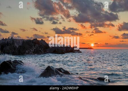 Coucher du soleil avec les nuages et le soleil juste au-dessus de l'horizon à Tropea plage avec des vagues se brisant sur les roches Banque D'Images