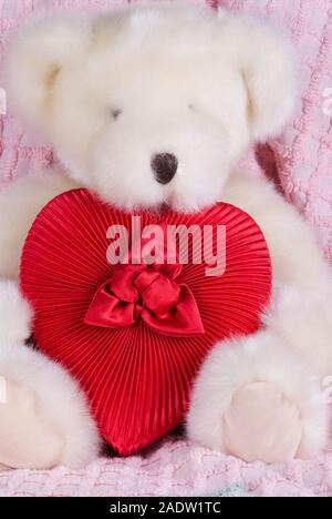 Peluche ours blanc en peluche animal est la tenue d'une boîte rouge en forme de coeur. Il est assis sur un ancien couvre-lit en chenille de couleur rose. Banque D'Images