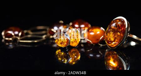 Panorama de bijoux avec des pierres d'ambre Collier en ambre, bague et boucle d'oreille et pendentif avec noble métal comme l'or, en face d'un fond noir sur un bla Banque D'Images