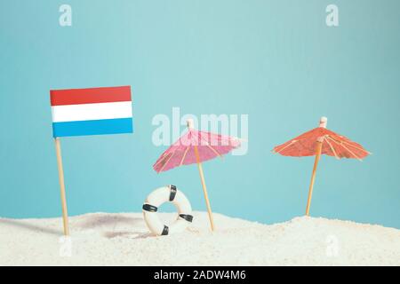 Drapeau Miniature de Luxembourg sur la plage avec parasols colorés et conservateur de vie. Concept de voyage, thème d'été. Banque D'Images