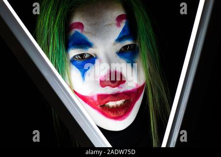 Fille avec un maquillage de clown rire follement sur le fond sombre. Banque D'Images