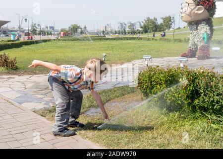 Garçon jouant avec de l'eau dans sprinkler, dans le parc. Kid mouille ses mains dans la fontaine. Banque D'Images