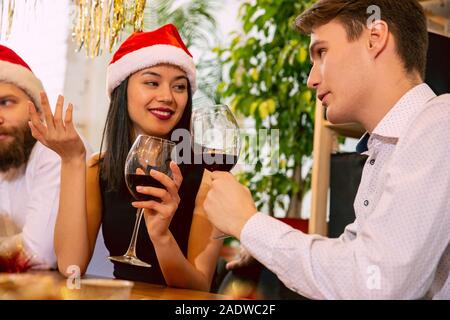 Heureux collègues tout en célébrant la nouvelle année de l'entreprise et fête de Noël. Les jeunes gens de race blanche en tenue de fête, parler boire du vin, Cheers. Concept de l'office de la culture, de l'équipe, l'amitié, de l'hiver. Banque D'Images