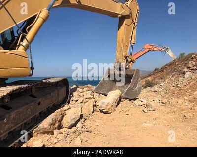 Déménagement pelles un rocher rochers au cours de la construction de routes sur le sol rocailleux. Les machines lourdes au terrassement, creusement, d'excavation. Banque D'Images