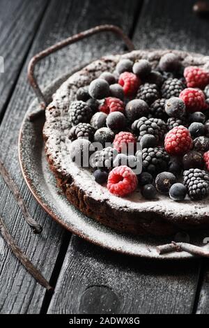 Kladdkaka dessert traditionnelle scandinave. Gâteau au chocolat sans gluten avec des framboises, mûres et de réglisse sirop dans vintage metal plat sur Banque D'Images