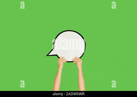 Mains tenant le signe de commentaire sur green studio arrière-plan. L'espace négatif pour le texte ou l'image, la publicité. Médias sociaux, montrant un sens, communication, gadgets, les technologies modernes. Bulle. Banque D'Images