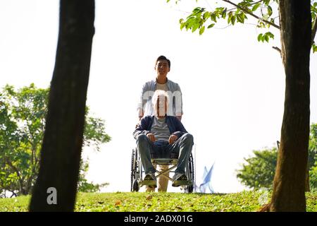 Les jeunes adultes d'Asie et son père en fauteuil roulant de profiter de la nature park Banque D'Images