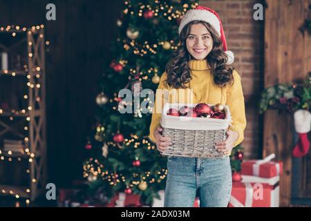 Photo de charmante dame mignon holding box avec des jouets de Noël en portant des boules de denim jeans red hat chandail jaune Banque D'Images