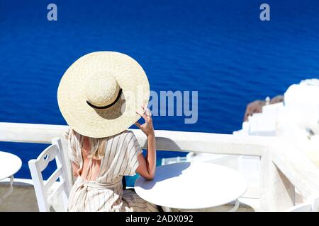 Jeune femme en robe blanche et chapeau de paille, balade dans la ville de Oia, Santorin, Grèce. Concept de loisirs, tourisme, voyages, vacances, r Banque D'Images