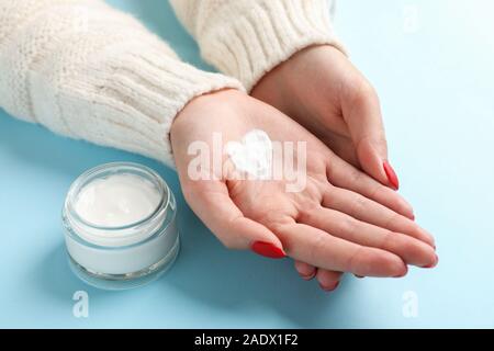 Femme mains, forme de cœur créé à partir de l'hiver, pot de crème pour la peau crème d'hiver sur fond bleu. Un espace réservé au texte