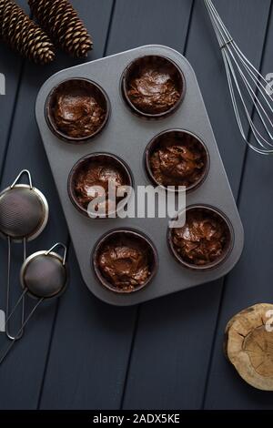 Hygge pâtisserie maison. Mêlée crue pour le chocolat muffins dans plaque de métal avec des ustensiles de cuisine sur fond sombre vue de dessus copyspace Banque D'Images