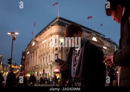 Deux utilisateurs d'un téléphone à l'étranger vérifier les messages en face de l'Trocadéro à Piccadilly Circus, le 22 novembre 2019, à Westminster, Londres, Angleterre. Banque D'Images