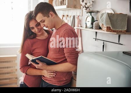 Cute couple reading book ensemble à la maison dans la cuisine dans la journée Banque D'Images