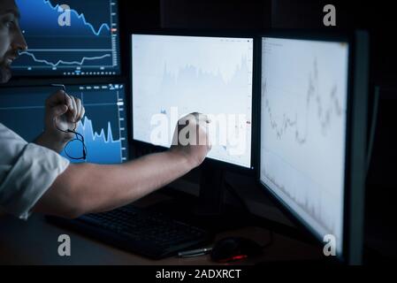 Concentré dans son travail. Homme barbu en chemise blanche travaille au bureau avec plusieurs écrans d'ordinateur dans les tableaux d'index Banque D'Images