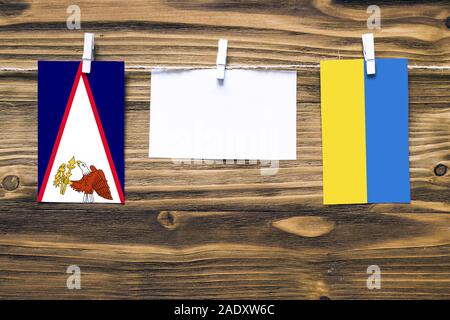 Drapeaux suspendus des Samoa américaines et de l'Ukraine attache à corde avec pinces à linge avec de l'espace de copie sur papier blanc sur fond de bois.rel diplomatique Banque D'Images