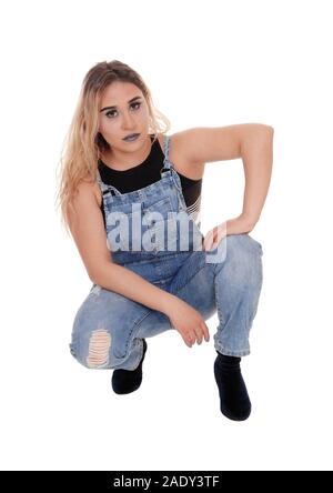 Une belle jeune femme blonde en jeans de travail accroupi sur le plancher dans le studio, isolée pour fond blanc Banque D'Images