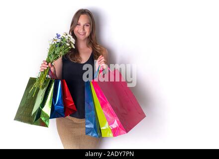 Une fille enceinte installée contre le mur avec des fleurs et les sacs du magasin. Joyful woman holding shopping bags bouquet de fleurs Banque D'Images