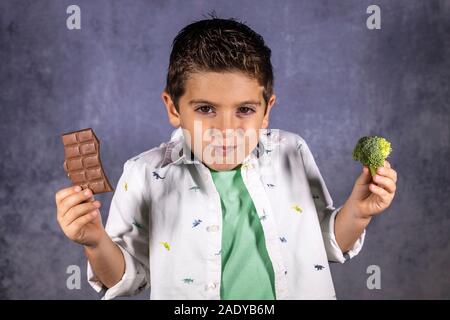 Petit enfant de choisir entre le brocoli et le chocolat Banque D'Images