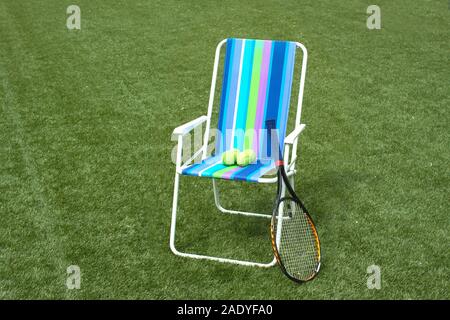 Fauteuil Métal et raquette de tennis avec quatre billes jaunes sur gazon synthétique surface cour vert Banque D'Images