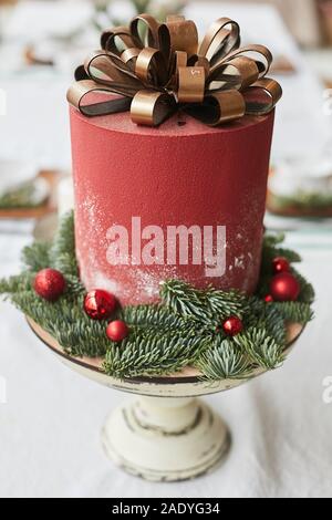 Gâteau de Noël rouge avec des rubans d'or au chocolat sous la forme d'arc décoré avec des boules rouges et de branches sur le support en bois. Pâtisserie pour le nouvel an Banque D'Images