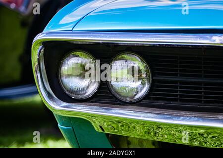 Selective focus sur une vieille voiture américaine vintage bleu musculaire la moitié avant, côté gauche, projecteurs lampes de close up avec cadre chrome et noir auvent Banque D'Images