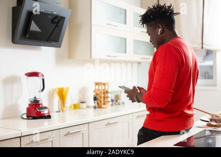 Jusqu'à la taille de l'homme debout à côté de la table de la cuisine et l'aide de gadgets modernes Banque D'Images