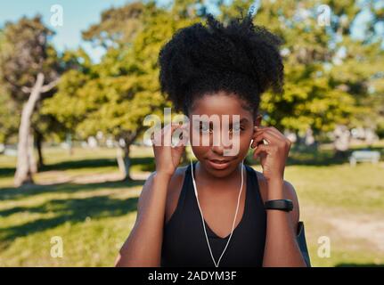 Portrait d'une femme confiante african american runner d'écouter de la musique sur l'athlète dans le parc d'écouteurs Banque D'Images