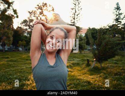 Portrait of a smiling sporty woman stretching her arms dans le parc Banque D'Images