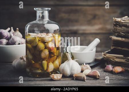 Huile aromatisée à l'ail ou de l'infusion aromatique bouteille et gousses d'ail. Mortier, vieux livres de recettes, couteau de cuisine. La cuisson à l'ail. Banque D'Images