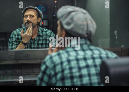 L'homme attentif de toucher sa barbe tout en étant dans barber shop Banque D'Images
